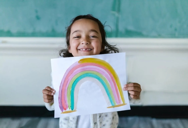A happy child holding up a drawing of a rainbow