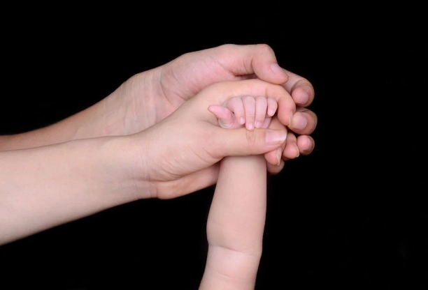 Two adult hands holding a baby hand