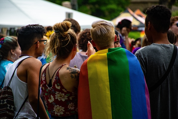 A group of young people looking into the distance, one with a rainbow flag on their back