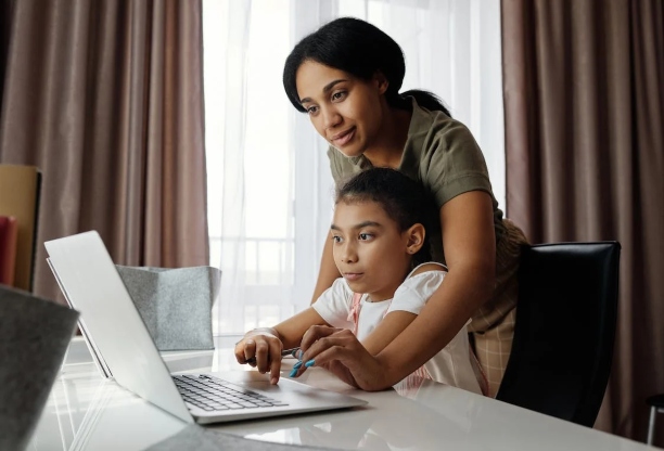 An adult woman helping a young girl using a laptop