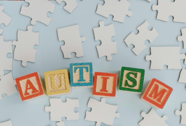Children's building blocks spelling the word AUTISM with various jigsaw pieces in the background