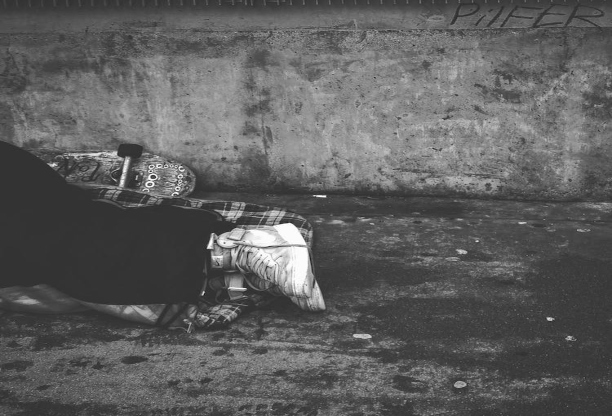 A black and white photo that shows part of someone's shoes and coat, clearly sleeping in the street