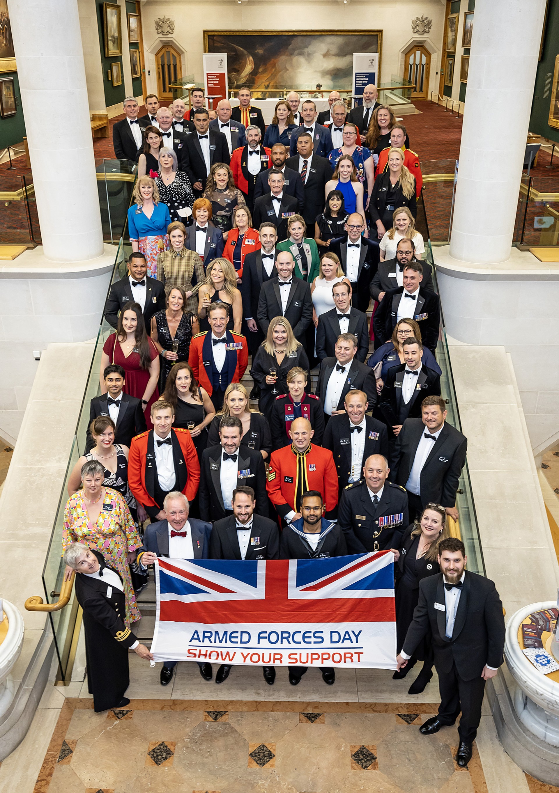 Attendees standing on the stairs of the building, holding an 'ARMED FORCES DAY - SHOW YOUR SUPPORT' flag.