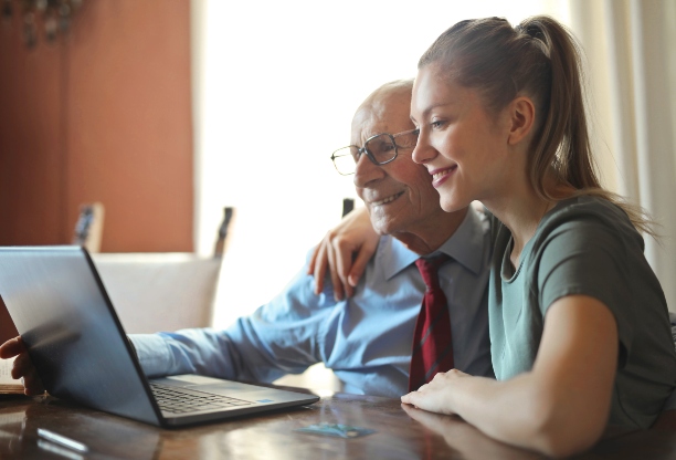 A young woman helping an older man with his computer