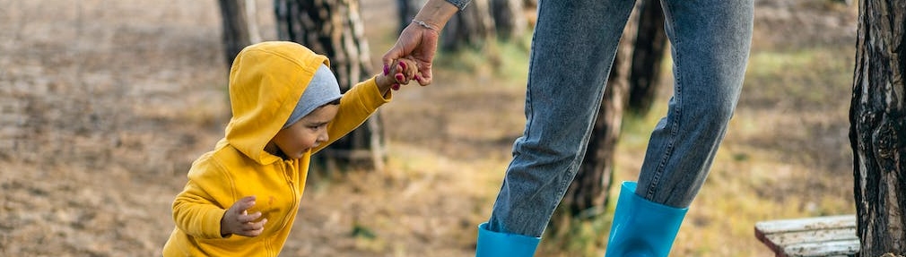 Small boy in yellow coat holding an adults hand whilst walking in the woods