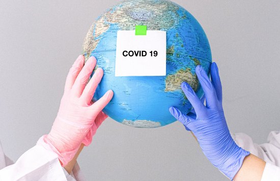 Globe being held aloft by two white coated people with label 'Covid' 