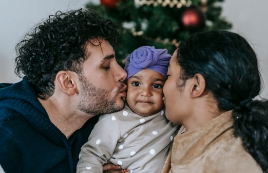 Stock image of a mother and father kissing their child.