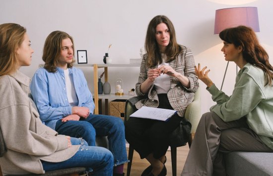 Stock image of three women and one man sat down in discussion.