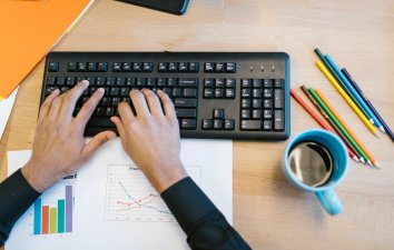 Keyboard on desk with hands over keys with mug of coffee and pencils alongside